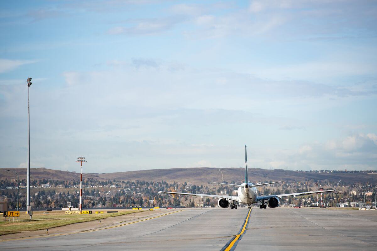 A commercial airplane taxis down the runway at an airport with hills and a cityscape in the background.